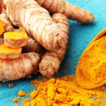 Kurkuma: Knollen und orangefarbenes Kurkumapulver auf hellblauem Grund.